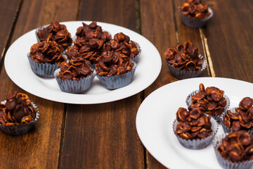 Chocolate cornflake cookies served on white plates. Chocolate cornflake cake in blue paper cupcake case