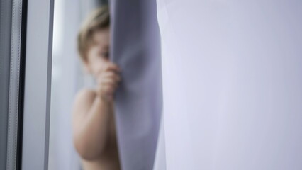 Blurred clip of toddler baby boy hiding behind curtain playing hide and seek