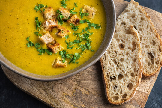 Zucchini cream soup. The dish is on a cutting board with two pieces of bread. Top view.