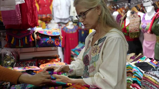 Mature woman tourist wearing ethnic clothes shopping for purse in a souvenir shop in Merida, Yucatan, Mexico.