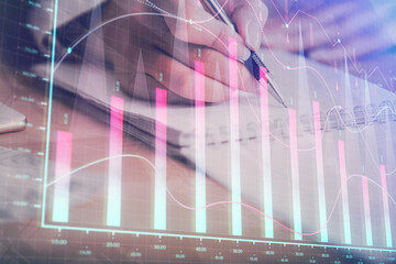 A woman hands writing information about stock market in notepad. Forex chart holograms in front. Concept of research. Multi exposure