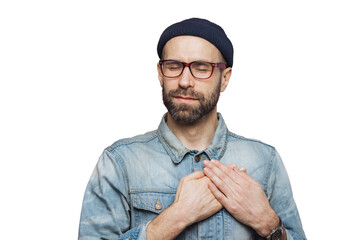 Pleased bearded man with closed eyes, keeps hands on chest, dressed in fashionable clothes, isolated over pink studio background. Middle aged male with shut eyes, expresses his love and sympathy