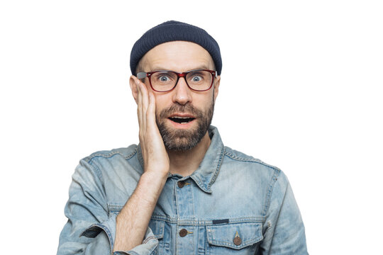 Portrait of amazed bearded excited male looks with surprisment in camera, recieves unexpected news, dressed in fashionable clothing, has attractive look, isolated over white studio background