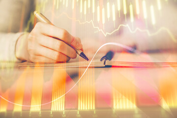 Fototapeta premium Hands writing information about stock market in notepad. Forex chart holograms in front. Concept of research. Multi exposure
