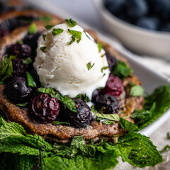 Blueberry tart on chocolate puff pastry; garnished with mint and a scoop of vanilla ice cream.