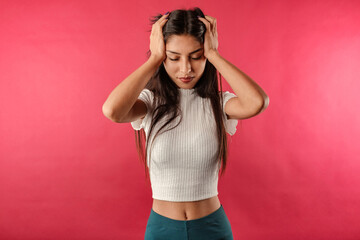 Young dark-haired woman wearing ribbed crop isolated over red background suffering from headache desperate and stressed because pain and migraine. Hands on head. Chronic daily headaches.