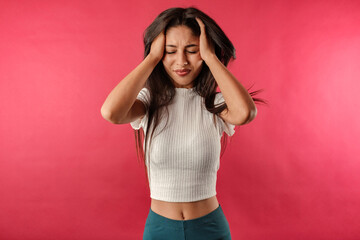 Brown-haired woman wearing white ribbed crop isolated over red background suffering from headache desperate and stressed because pain and migraine. Hands on head. Very sad headache.