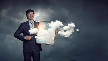 Man holding frame with blue sky and clouds