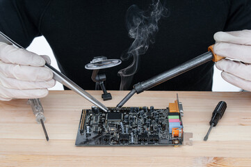Repairman in gloves soldering circuit board of electronic device on the table