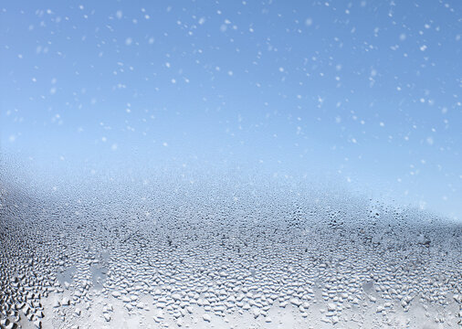 Water drops and snow on the wet window glass. Abstract background.