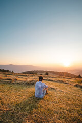 Man in shirt resting on grass watching sunset on a mountain in Beskydy mountains, Czech republic. Soaking up positive energy and relieving stress