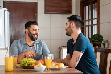 Fototapeta na wymiar brazilian gay couple having breakfast and talking in kitchen table