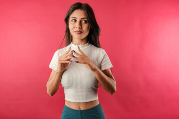 Portrait of brunette woman wearing white ribbed crop isolated over red background cunningly...