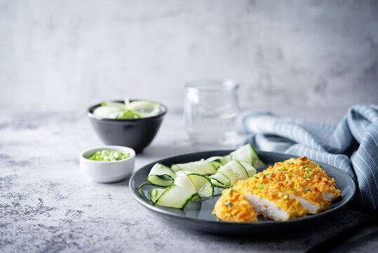 Bread Crumbs Cheesy Chicken Breast With Cucumbers In A Plate