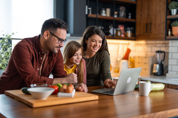 Fototapeta premium Happy family searching for delicious recipes online while standing in the kitchen.
