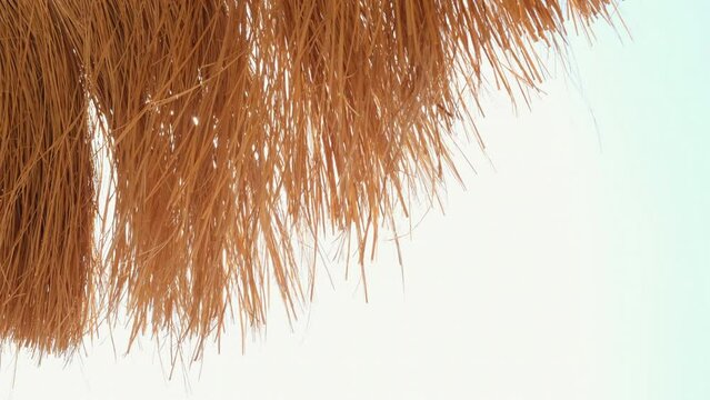 Bottom view on beach straw umbrella against the blue sky on the beach.