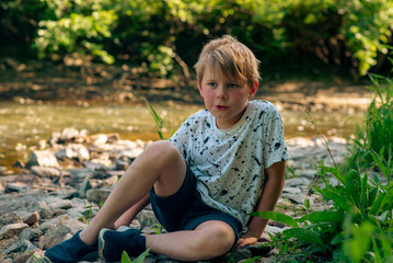 a boy of nine years old near a small river in summer