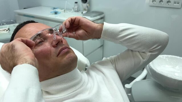 handsome adult man wears transparent glasses in the dental chair so that sand from the sandblaster does not get into his eyes for cleaning his teeth he is waiting for the doctor