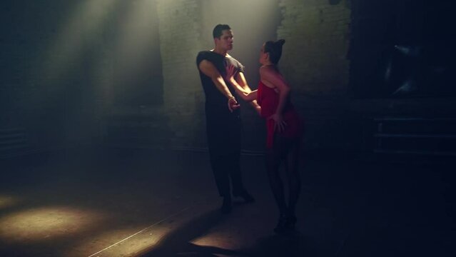 Side view ballroom dancers dancing passionate tango face to face, approaching each other,man takes woman by hand, lunges,presses her to him,she makes foot swing to side,dance support. Loft atmosphere.