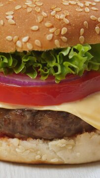 Vertical shot. On a white background, a close up of a sandwich with a burger patty, blue onion, lettuce, and tomato.