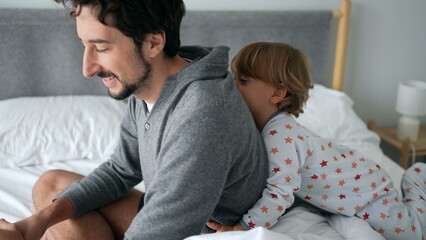 Cute baby toddler climbing on father back in the morning bed