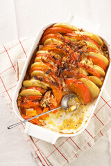 Sliced and layered potato and pumpkin casserole in a white baking form on marble background, topped with roasted onions, feta cheese crumbs and whipped cream