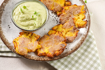 Trendy comfort snack crispy roasted crushed potatoes on a round plate with creamy avocado and garlic dip on a green checkered kitchen towel