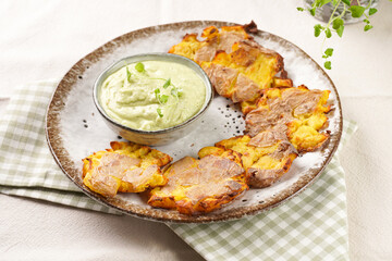 Trendy comfort snack crispy roasted crushed potatoes on a round plate with creamy avocado and garlic dip on a green checkered kitchen towel