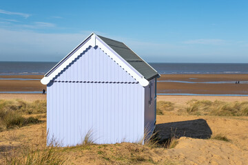 Traditional wooden beach hut in the sand dunes on a bright and sunny day on Hunstanton beach, North Norfolk coast.