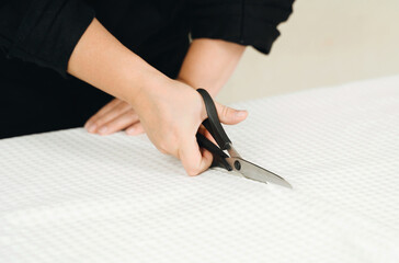 A woman seamstress cuts a white fabric on the table.