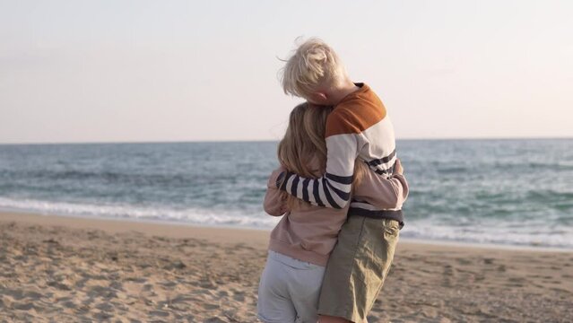 The older brother hugs his beloved younger sister tightly on the beach by the sea.