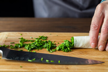 Chopped chives on a wooden cutting board with a sharp knife in front