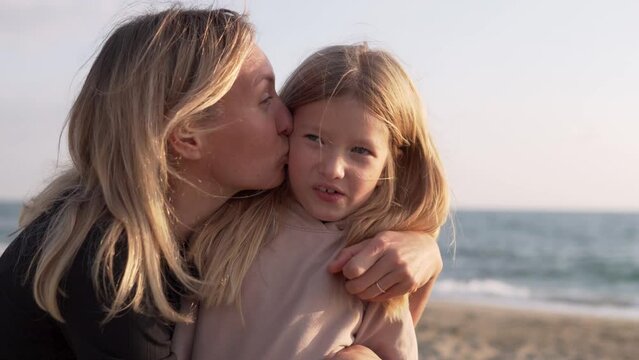 Beautiful Mother kisses her beloved daughter against the background of the sea. Family hugs, reunion of mother and daughter.