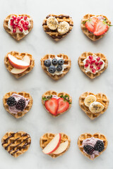 Several mini heart shaped waffles with various toppings.
