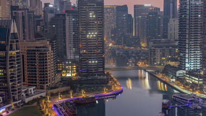 Dubai Marina with several boats and yachts parked in harbor and skyscrapers around canal aerial night to day timelapse.