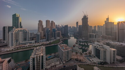 Dubai Marina with several boats and yachts parked in harbor and skyscrapers around canal aerial all day timelapse.