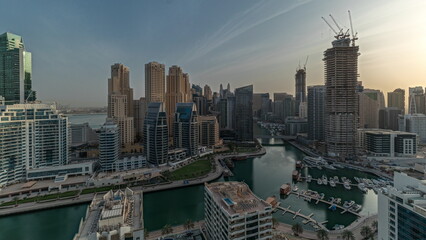 Panorama showing Dubai Marina with several boats and yachts parked in harbor and skyscrapers around canal aerial morning timelapse.