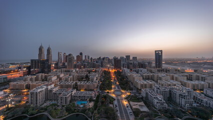 Obraz premium Panorama of skyscrapers in Barsha Heights district and low rise buildings in Greens district aerial night to day timelapse.