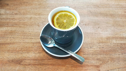 Hot lemon tea with a slice of a lemon in a glass and a spoon at the table.