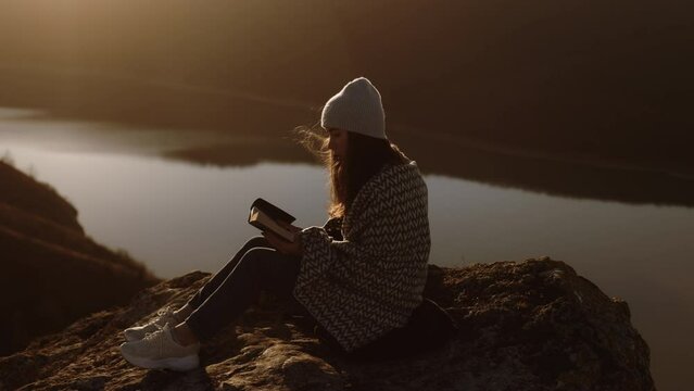 The woman opens the Bible, prays. A girl reads the Bible in the open air, studies the word of God at sunset on top of a mountain. Finding Truth in the Scriptures.
