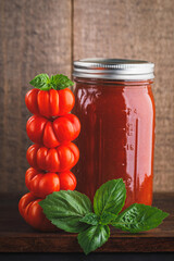 Jar of home canned tomato sauce and stack of costoluto genovese tomatoes topped with basil leaves