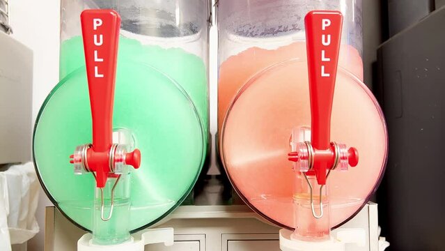 Machines are preparing icy slushy drinks by stirring colorful sweet ice