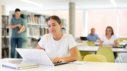 Young female European student studying with a laptop in the library