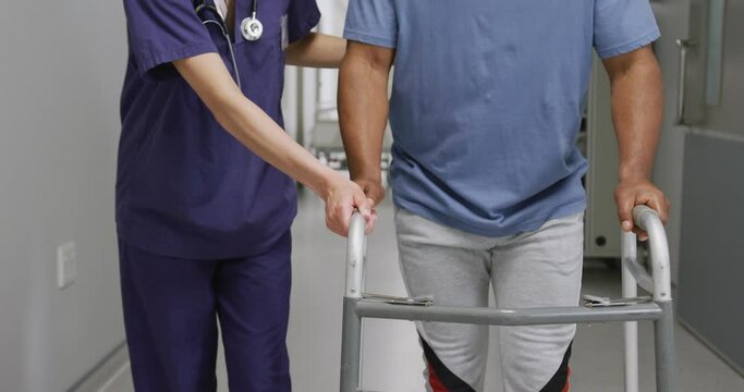 Midsection of diverse female doctor helping male patient use walking frame at hospital