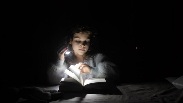 a girl reads a book illuminating herself with a flashlight in a dark room without light
