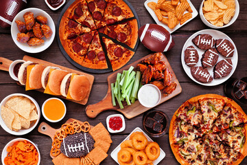 Super Bowl or football theme food table scene. Pizza, hamburgers, wings, snacks and sides. Overhead...