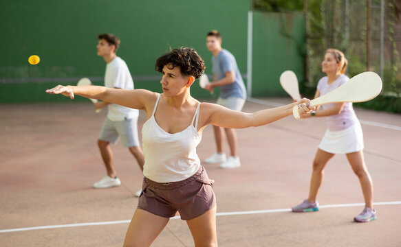 Latin woman serving ball with paleta during Basque pelota game outdoors. Woman playing pelota on outdoor fronton.