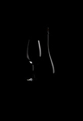 Elegant red wine glass and a wine bottle  with red cherry isolated on the black background. bottle silhouette