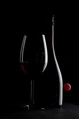 Elegant red wine glass and a wine bottle  with red cherry isolated on the black background. bottle silhouette