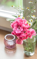 A small bouquet of poza geranium flowers and a berry-colored candlestick